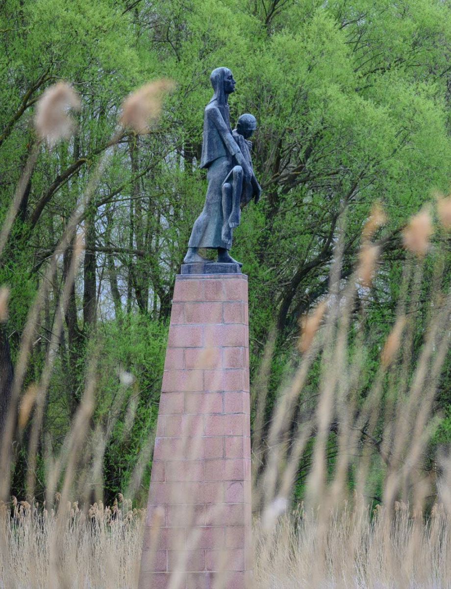 Ein Manmahl der Gedenkstätte Ravensbrück am Ufer der Havel. Im Vordergrund wehen Gräser im Wind.